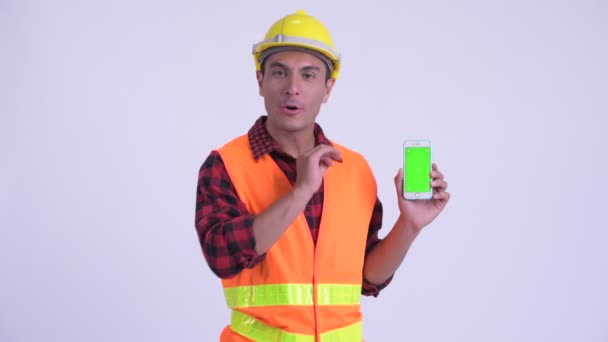 Young happy Hispanic man construction worker talking while showing phone — Stock Video