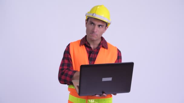 Jovem feliz homem hispânico trabalhador da construção pensando ao usar laptop — Vídeo de Stock