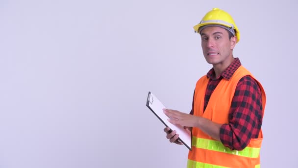 Joven feliz hispano trabajador de la construcción mostrando portapapeles y dando pulgares hacia arriba — Vídeos de Stock