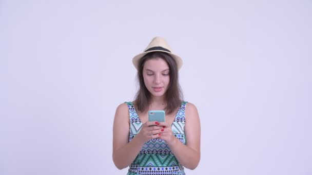 Twarz szczęśliwej młodej pięknej kobiety turysty za pomocą telefonu i patrząc zaskoczony — Wideo stockowe