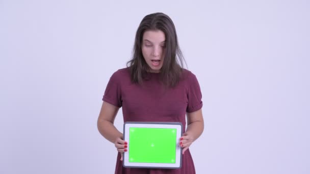 Молодая красивая беременная женщина показывает цифровой планшет и выглядит потрясенным — стоковое видео