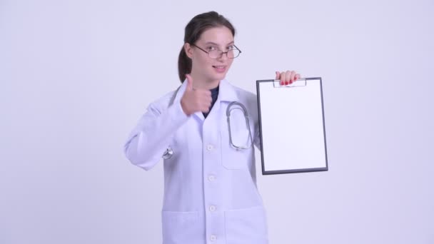 Happy young beautiful woman doctor showing clipboard and giving thumbs up — Stock Video