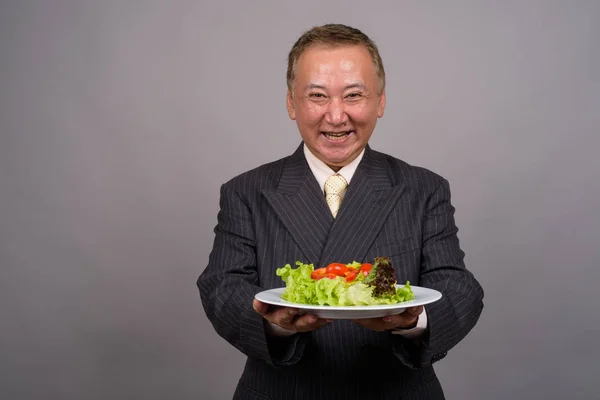 Portret van rijpe Aziatische zakenman tegen de grijze achtergrond — Stockfoto