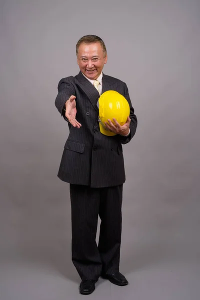 Зрілі азіатського будівництва бізнесмен проти сірого фону — стокове фото