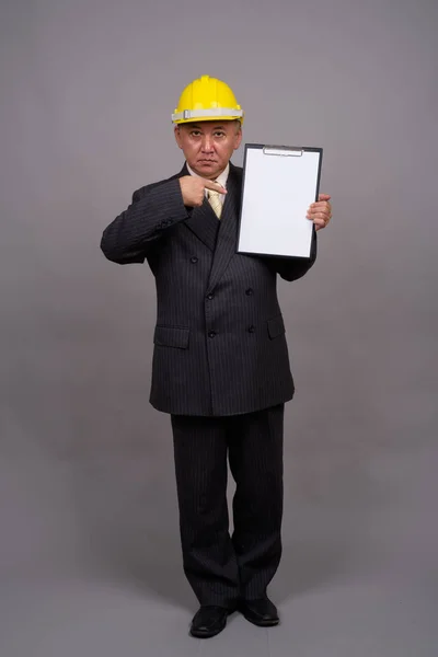 Obchodník s vyspělým asijským stavebním obchodníkem na šedé pozadí — Stock fotografie