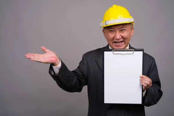 Mature Asian construction businessman against gray background — Stock Photo, Image