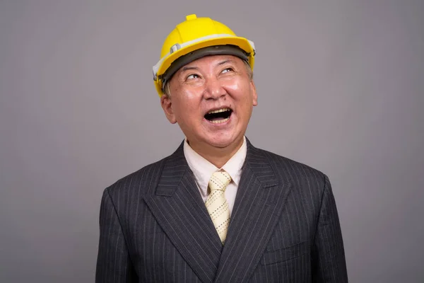 Mature Asian construction businessman against gray background — Stock Photo, Image