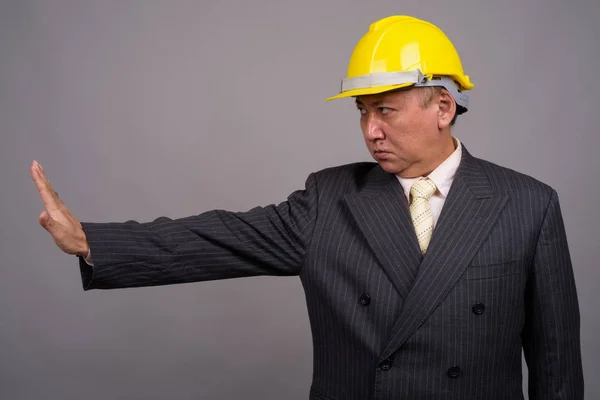 Mature Asian construction businessman against gray background — Stock Photo, Image