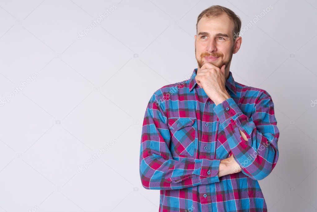 Portrait of happy young bearded hipster man thinking