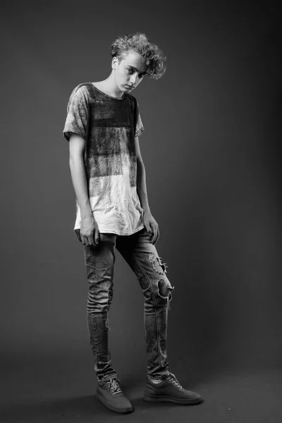 Skinny ung man med lockigt hår mot grå bakgrund i blac — Stockfoto