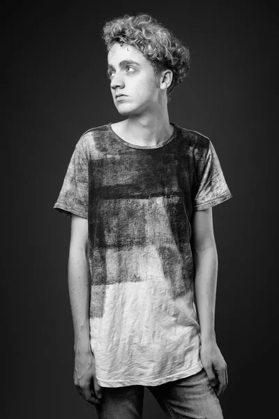 Skinny young man with curly hair against gray background in blac