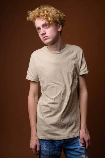 Skinny ung man med lockigt hår mot brun bakgrund — Stockfoto
