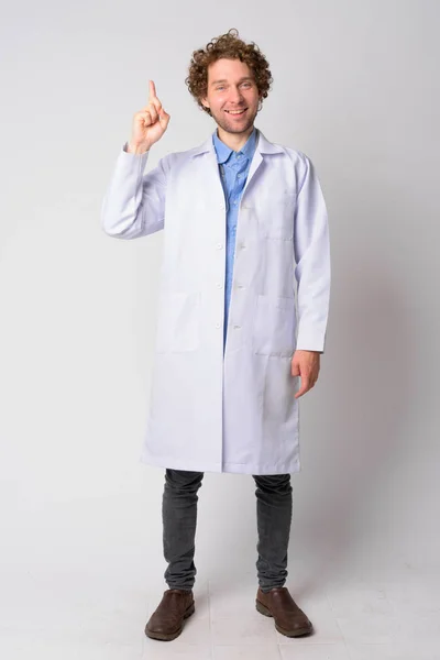 Full body shot of happy man doctor with curly hair pointing up — Stock Photo, Image