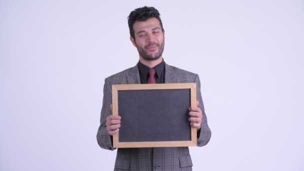 Happy bearded Persian businessman thinking while holding blackboard — Stock Video