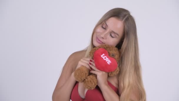 Young beautiful blonde woman in bikini with teddy bear acting childlike — Stockvideo