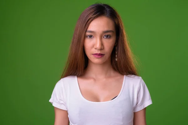 Young slim Asian woman against green background — Stok fotoğraf