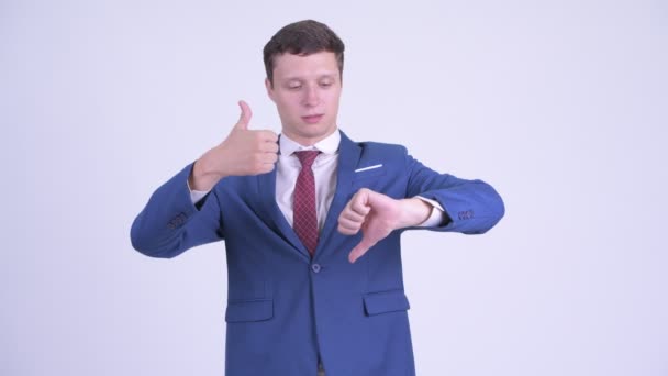 困惑的年轻商人在竖起大拇指和竖起大拇指之间选择 — 图库视频影像