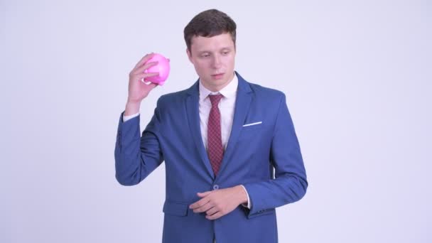 Estressado jovem empresário segurando porquinho banco e dando polegares para baixo — Vídeo de Stock