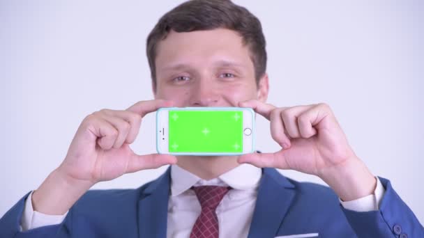 Gesicht eines glücklichen jungen Geschäftsmannes zeigt Handy — Stockvideo