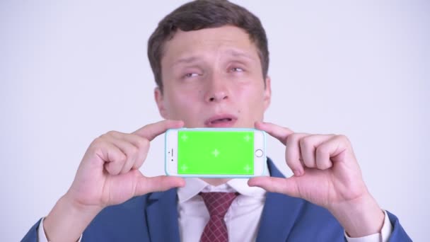 Gesicht eines glücklichen jungen Geschäftsmannes, der beim Vorzeigen seines Telefons denkt — Stockvideo