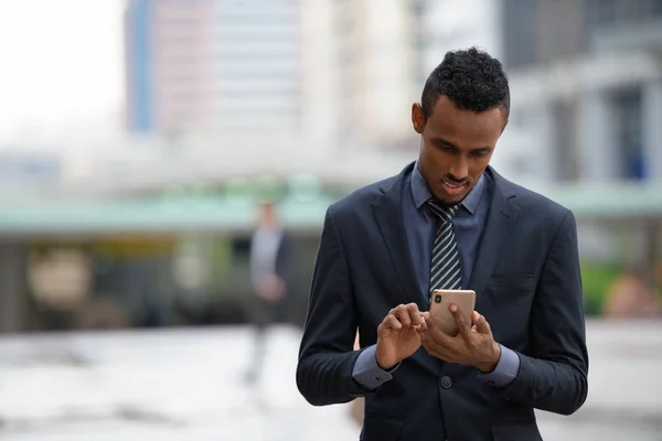 Happy young African businessman using phone in the city — Stock Photo, Image