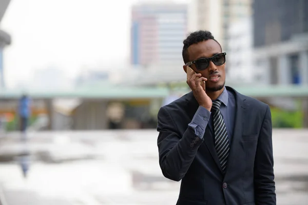 Ung afrikansk affärsman med solglasögon pratar i telefon utomhus — Stockfoto