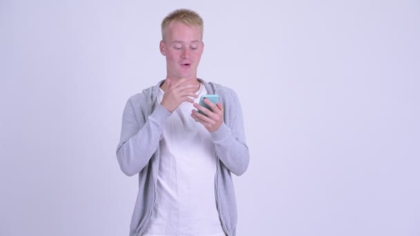 Szczęśliwy młody blond człowiek za pomocą telefonu i patrząc zaskoczony — Wideo stockowe