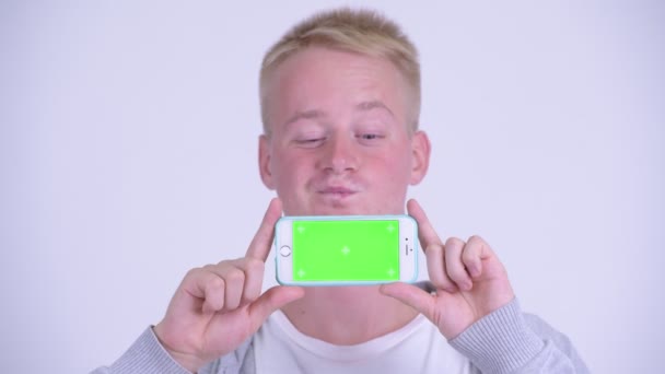 Face of happy young blonde man thinking while showing phone — Stock Video