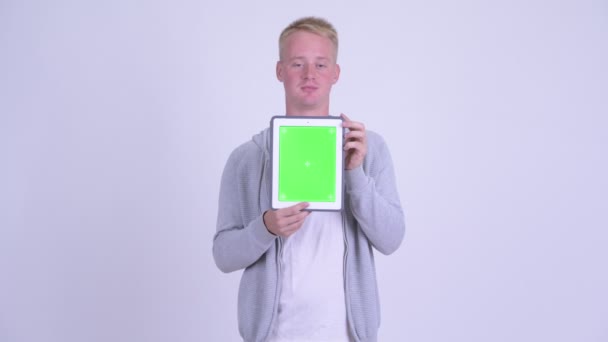 Happy young blonde man talking while showing digital tablet — Stock Video