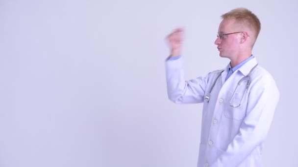 Sorprendido joven hombre rubio médico chasquido de los dedos y mostrando algo — Vídeo de stock