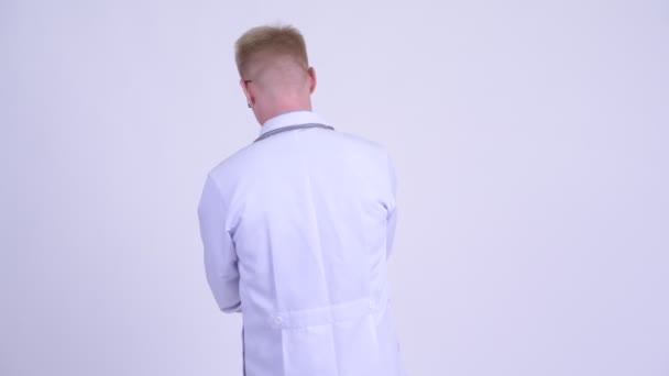 Happy young blonde man doctor turning around and waving hand — Stock Video