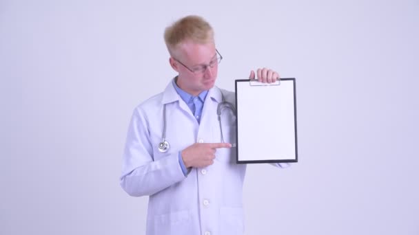 Happy young blonde man doctor showing clipboard and giving thumbs up — Stock Video