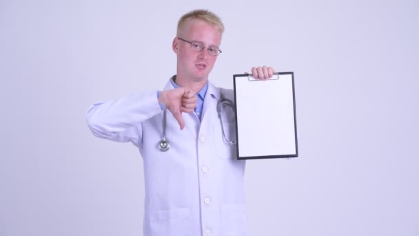 Serious young blonde man doctor showing clipboard and giving thumbs down — Stock Video