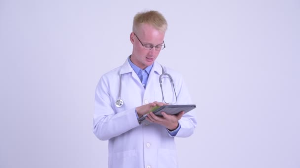 Молодой блондин врач говорит, показывая цифровой планшет — стоковое видео