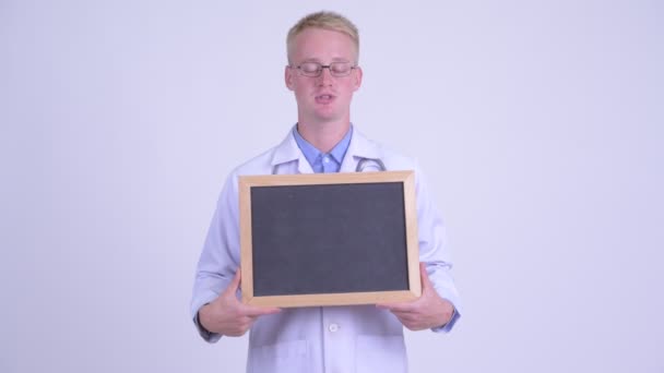 Happy young blonde man doctor talking while holding blackboard — Stock Video