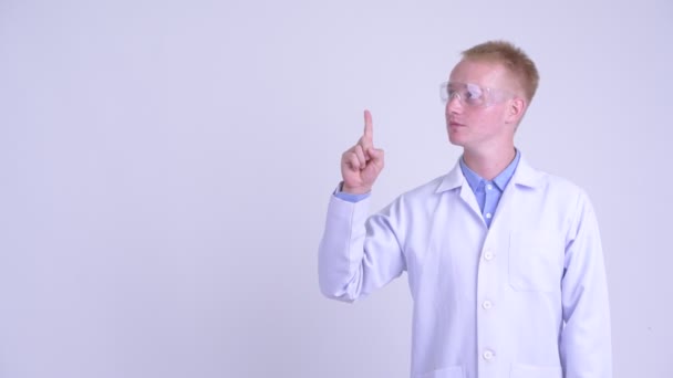 Happy young blonde man doctor with protective glasses thinking and pointing up — Stock Video