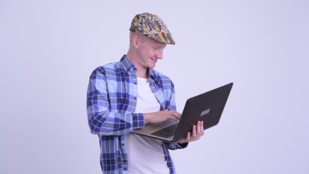 Happy young handsome hipster man thinking while using laptop — Stock Video