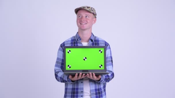 Jovem feliz hipster bonito homem pensando ao mostrar laptop — Vídeo de Stock