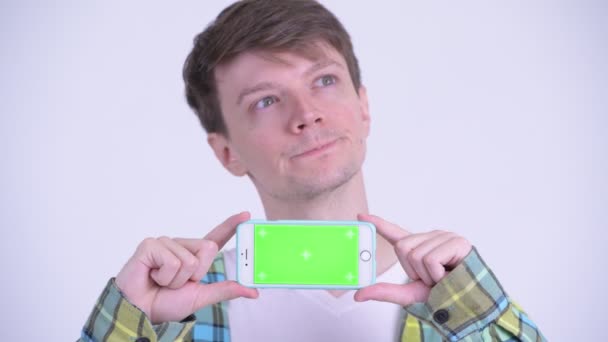 Cara de joven hombre guapo feliz pensando mientras se muestra el teléfono — Vídeos de Stock