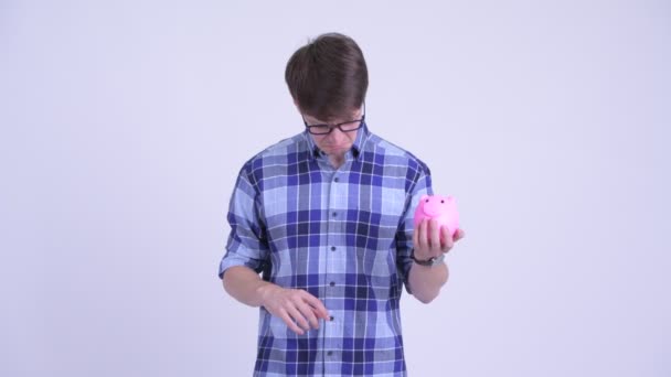 Stressed young hipster man holding piggy bank and giving thumbs down — Stock Video