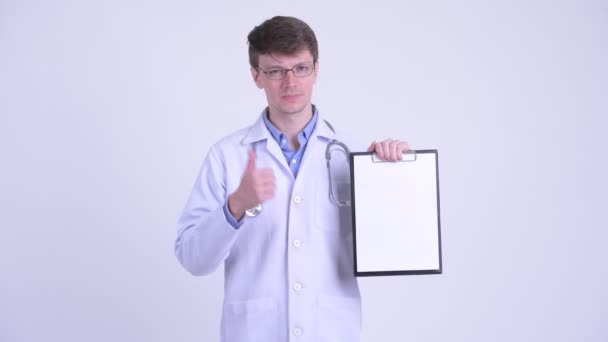 Šťastný mladý doktor ukazuje schránku a dává palce — Stock video