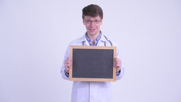 Happy young handsome man doctor holding blackboard — Stock Video