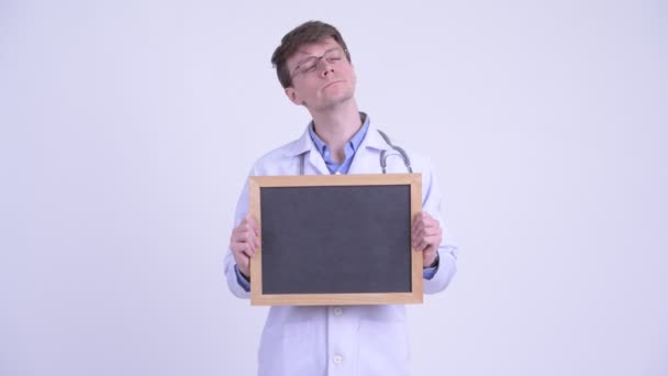 Happy young handsome man doctor thinking while holding blackboard — Stock Video