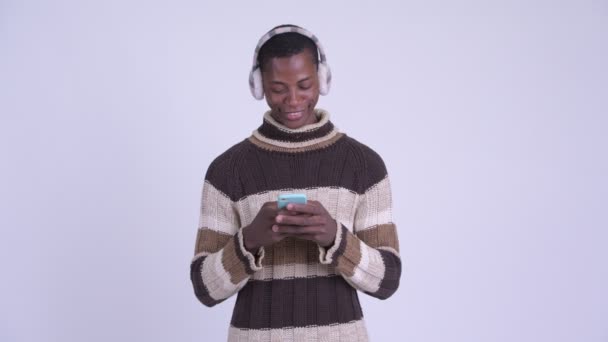 Jovem homem africano feliz pensando ao usar o telefone pronto para o inverno — Vídeo de Stock