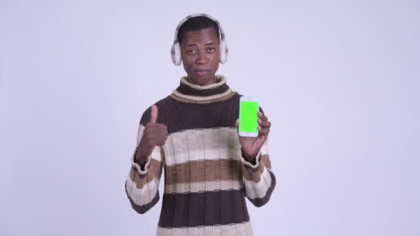 Νεαρός ευτυχισμένος Αφρικανός που δείχνει τηλέφωνο και δείχνει τους αντίχειρές του έτοιμους για το χειμώνα — Αρχείο Βίντεο