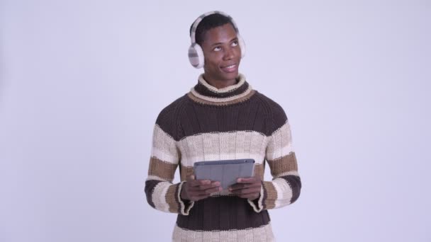 Ung glad afrikansk man tänker när du använder digital tablett redo för vintern — Stockvideo