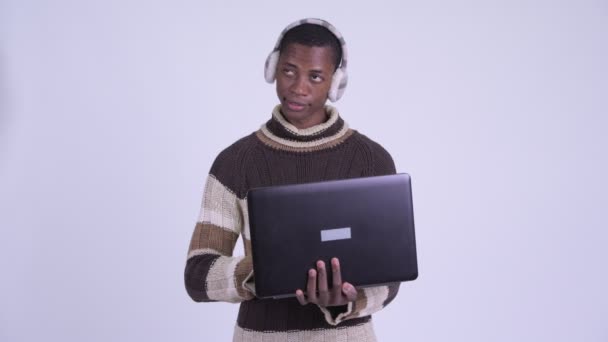 Genç mutlu Afrikalı adam kışa hazır dizüstü bilgisayar kullanırken düşünüyor. — Stok video