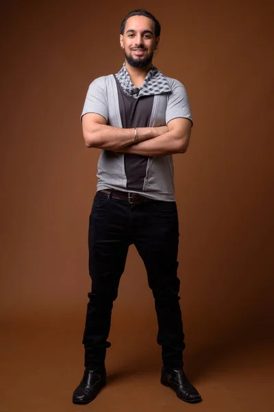 Young bearded Indian man against brown background