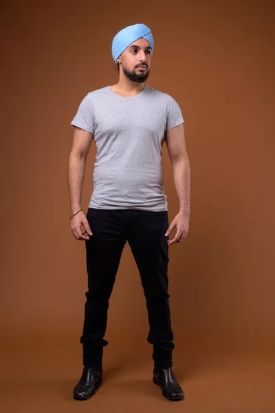 Young bearded Indian Sikh man wearing turban against brown backg — 스톡 사진