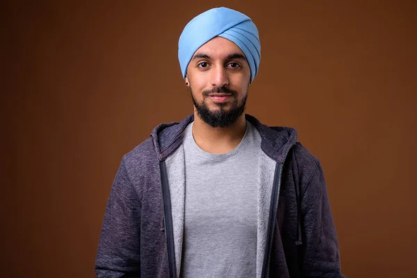 Ung skäggig indisk sikh man bär turban mot brun rygg — Stockfoto